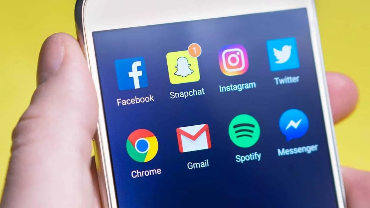 Hand holding a phone with social media icons floating around it